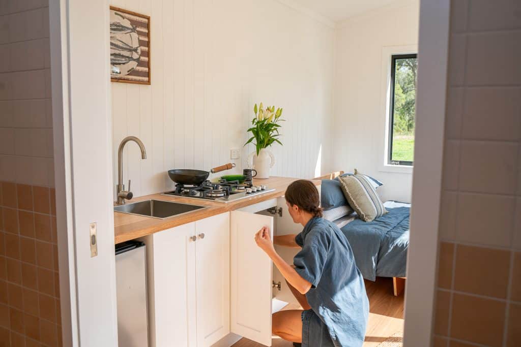 Kitchen and bedroom inside an Outhaus module, person at the benchtop