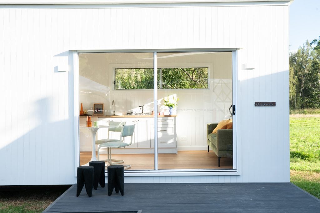 White Outhaus module with a deck and open sliding doors on rural land