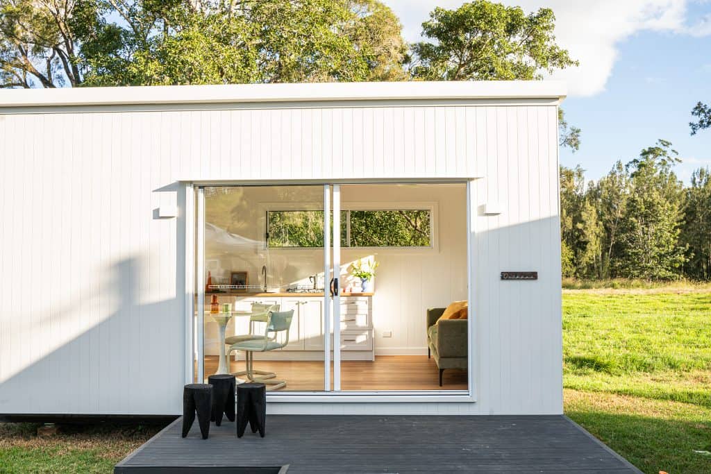 White Outhaus modular home with deck and open sliding doors in a rural setting
