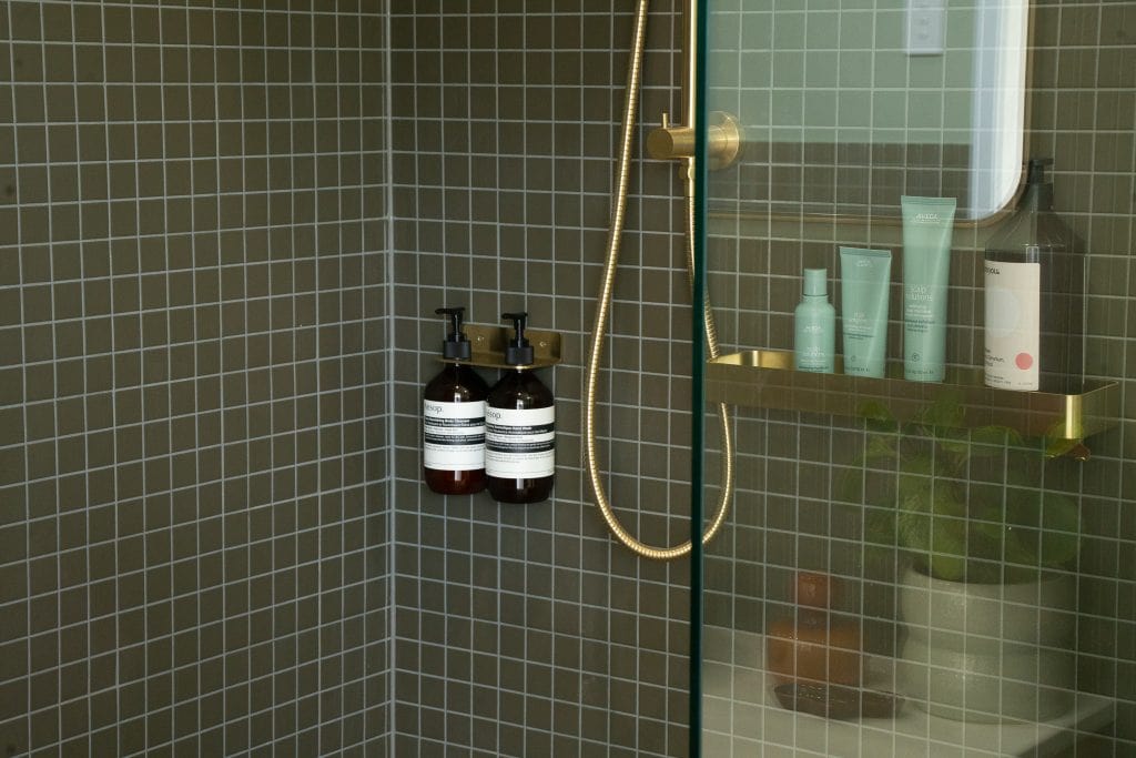 Green tiled shower with brass rail and glass screen in an Outhaus module